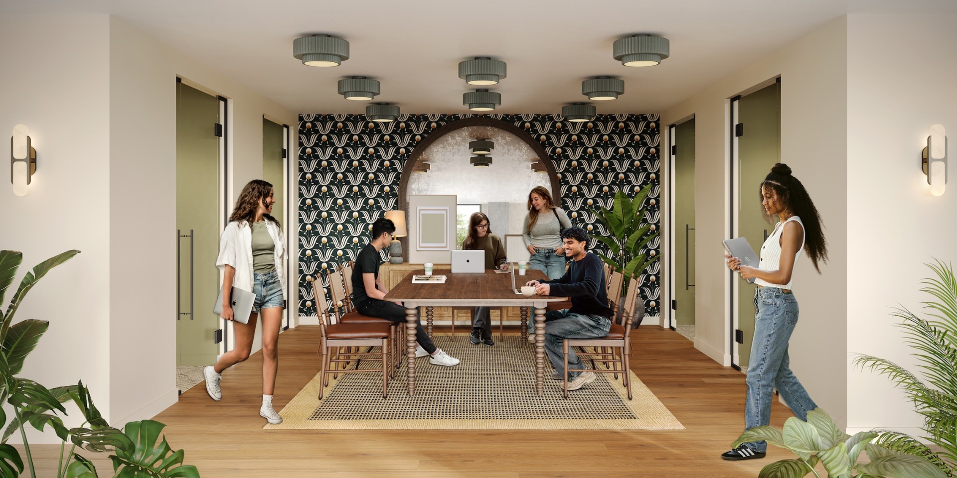 Six people are in The Jay’s modern office meeting room with a large wooden table, laptops, and plants. Some are sitting and working, while others stand or walk, engaging in discussion against a stylish patterned wall.