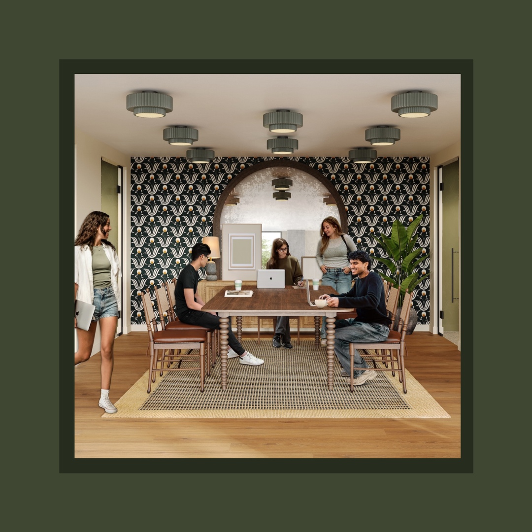 Five people are in a modern meeting room with a patterned accent wall, large arched mirror, wooden table and chairs—reminiscent of stylish off campus apartments TAMU students might enjoy. Some are standing, others seated, and two are using laptops.