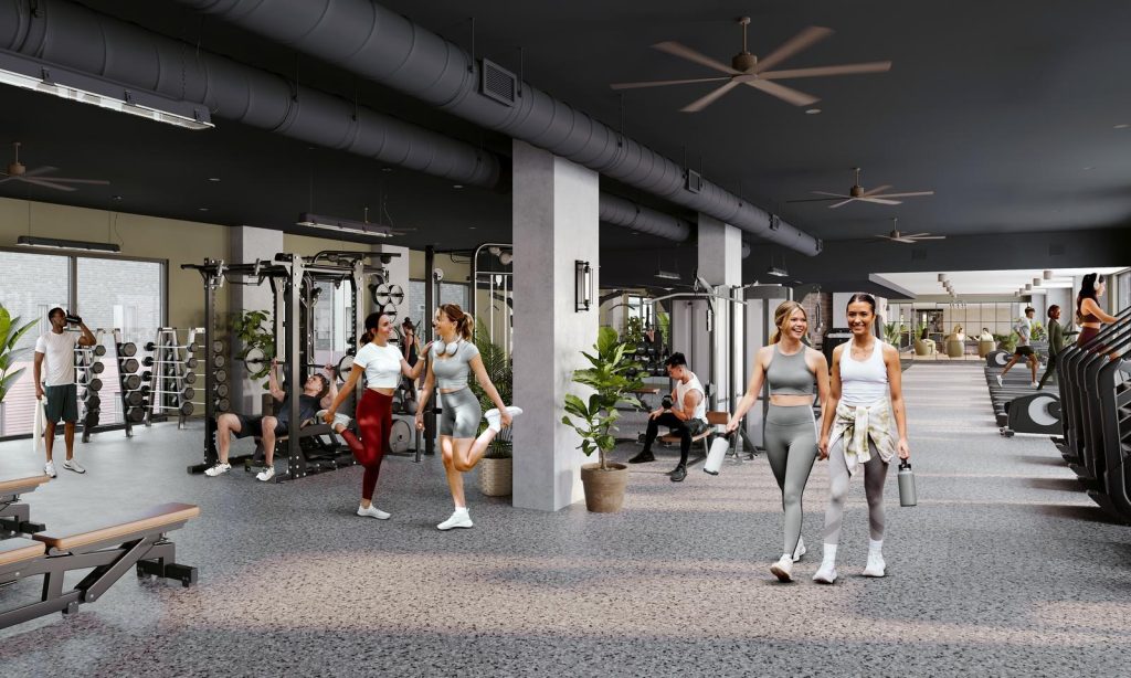 The Jay's spacious gym with people working out on various equipment, stretching, and walking. The space is well-lit with fans, potted plants, and modern furnishings. Located near Texas A&M in College Station.