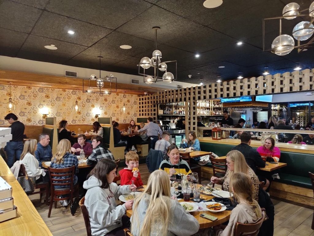 Inside Napa Flats Wood-Fired Kitchen includes booth and regular table seating backed by yellow trim and tiling with modern bubble-shaped chandeliers.