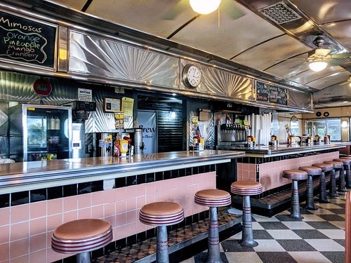 Classic diner finishes include a checkerboard floor, pink-and-black tile backsplash, tin accents over the kitchen and retro pink bar stools found in Hullabaloo Diner in College Station.