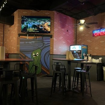 A classic pizza spot featuring high top tables inside with brick walls, murals, neon signs and TVs on the walls.