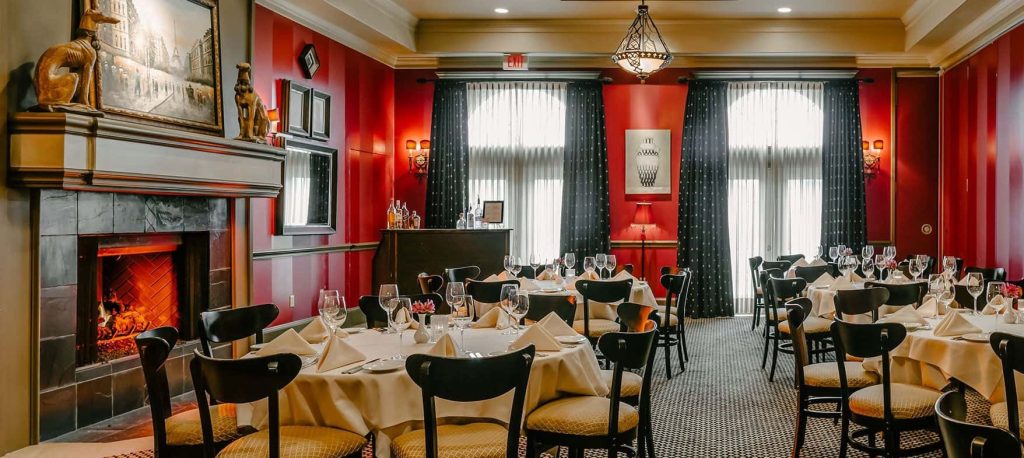 Elegant table-settings at Christopher’s World Grille with home-style interior featuring a fireplace, curtains and carpet.
