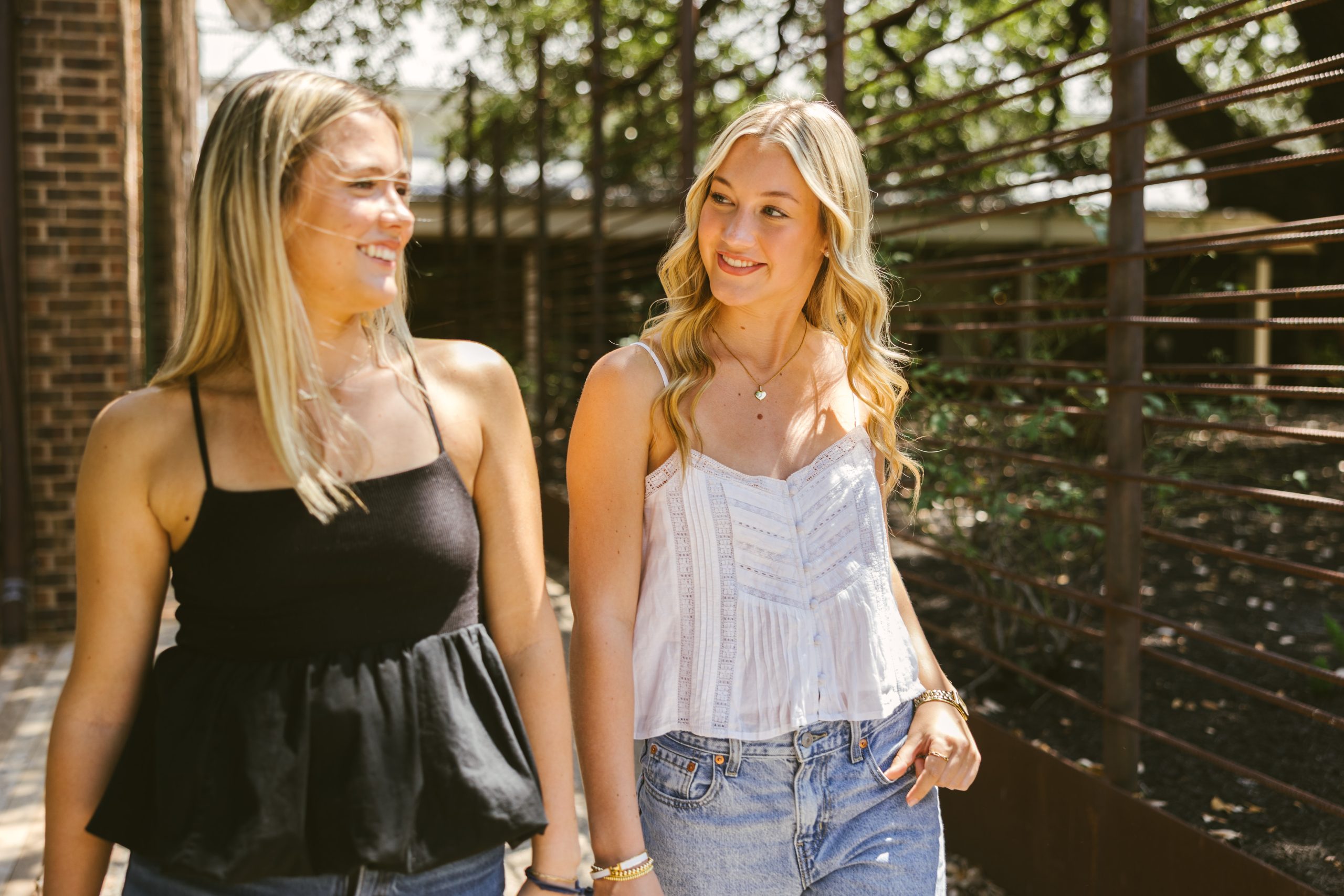 Two young women walking and smiling at each other outdoors.